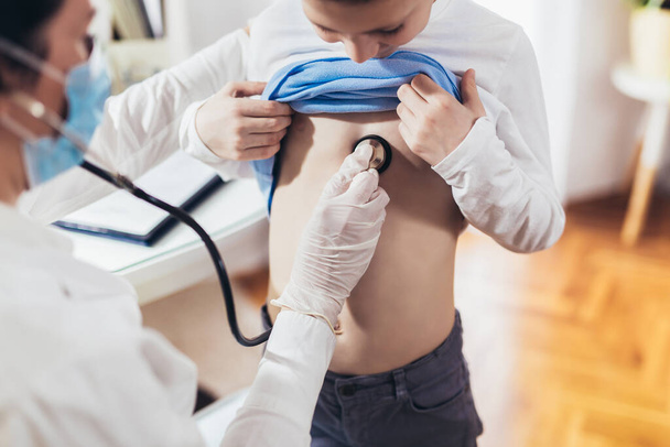 Dokter luistert naar de borst van de jongen met stethoscoop in zijn kantoor in het ziekenhuis - Foto, afbeelding