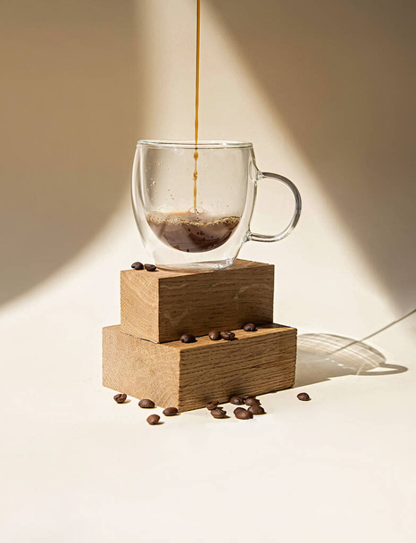 Glazen kopje koffie op een beige achtergrond giet in een mok. Minimalistische foto bij daglicht - Foto, afbeelding
