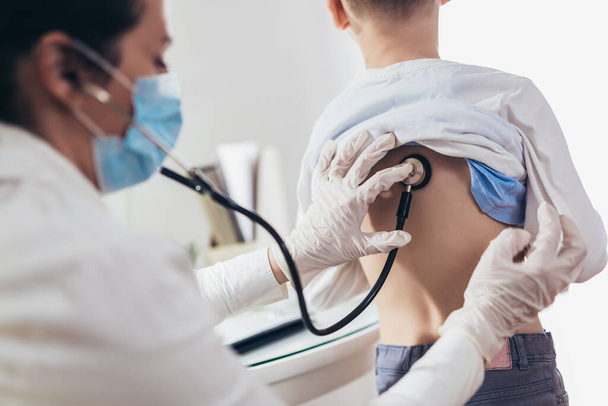 Lekarz słuchający klatki piersiowej chłopca ze stetoskopem w gabinecie w szpitalu. - Zdjęcie, obraz