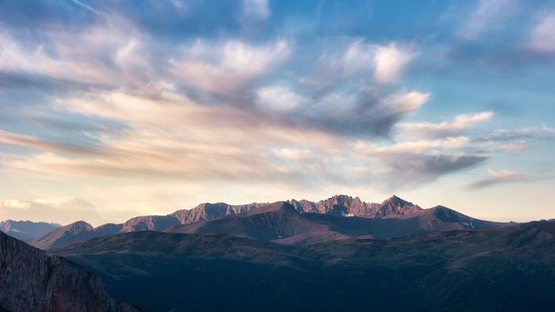 Chmury nad ostrymi skalistymi szczytami gór, oświetlone zachodzącym słońcem. Kaukaskie góry. Wysokiej jakości zdjęcie - Zdjęcie, obraz