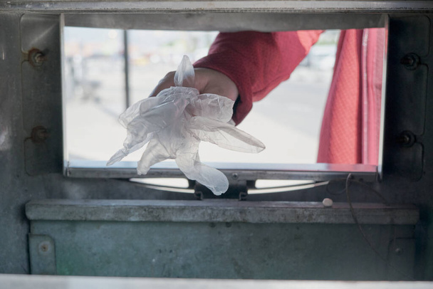 Woman hand throws protective gloves against the virus into the trash - Фото, изображение