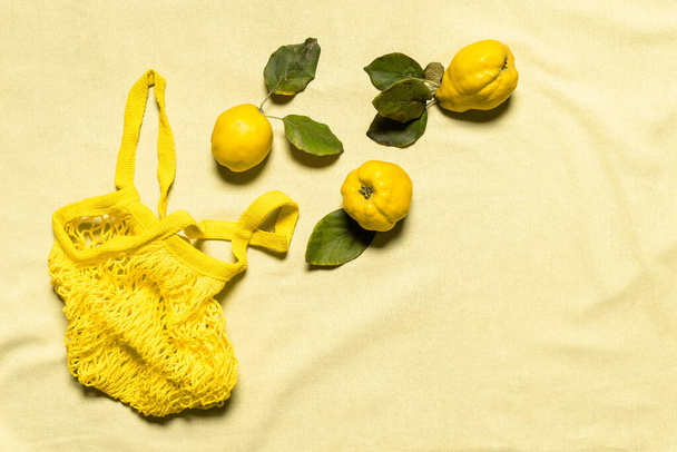 リンゴの葉が3枚としわのあるパステルカラーのリネンの背景に黄色のメッシュバッグ。有機果物には自然な欠陥があります。意識的な消費主義の概念。平置きだ。スペースのコピー. - 写真・画像