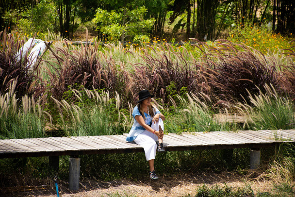 Οι ταξιδιώτες thai γυναίκες άνθρωποι κάθονται ποζάρουν πορτρέτο σε ξύλινη γέφυρα στον κήπο αυλή εξωτερική και ταξίδια επίσκεψη ξεκουραστείτε χαλαρώστε στο λιβάδι λουλούδι με τον άνεμο και το φόντο στο βουνό Kanchanaburi, Ταϊλάνδη - Φωτογραφία, εικόνα