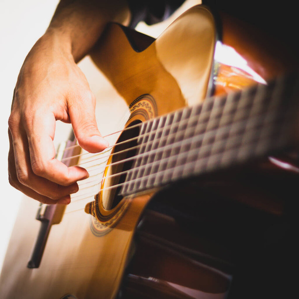 Main d'un musicien jouant une guitare acoustique en bois sur fond blanc et noir. Jeune guitariste - Photo, image