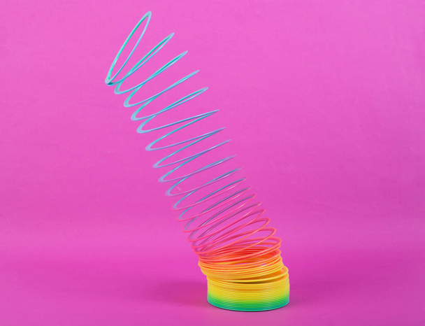 Pembe arka planda gerilmiş Gökkuşağı plastik, çok renkli spiral, ince çizgili oyuncak. Minimalizm - Fotoğraf, Görsel