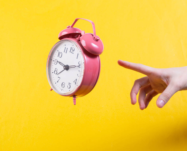Hand and Levitating pink alarm clock on yellow background. Minimalistic still life. Concept art - Photo, Image