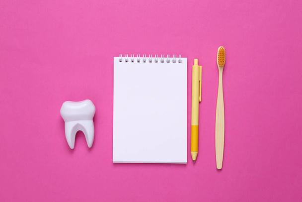 Cepillo de dientes de bambú ecológico, cuaderno y diente sobre fondo rosa. Concepto de cuidado dental - Foto, imagen
