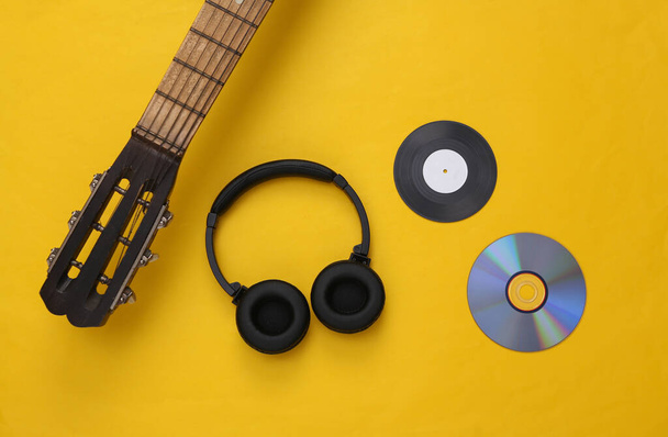 Layout musical. Guitarra acústica, fones de ouvido, disco de vinil e cd em fundo amarelo. Vista superior. Depósito plano  - Foto, Imagem