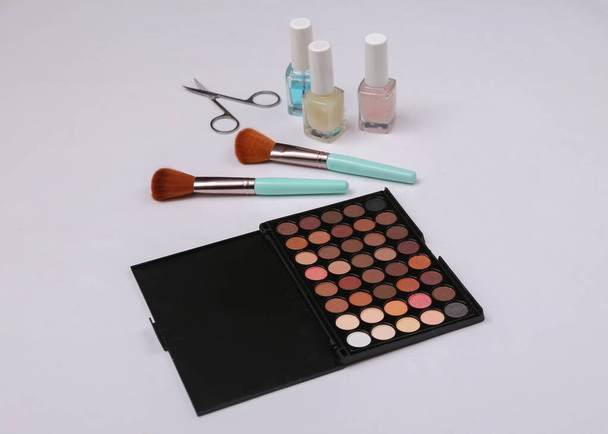 Beauty products on a white background. Make up eye shadow palette, makeup brushes, scissors and nail polish - Fotó, kép
