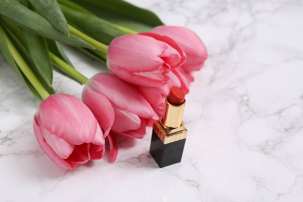 Lápiz labial y tulipanes rosados sobre fondo de mármol. Concepto romántico y de belleza - Foto, imagen