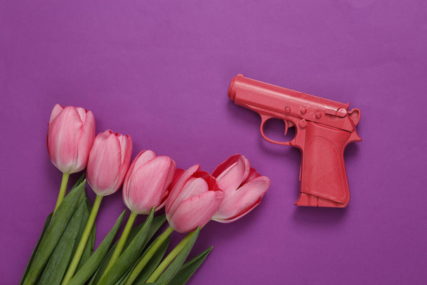 Pistola con tulipanes sobre fondo púrpura. Arte conceptual. Minimalismo - Foto, Imagen