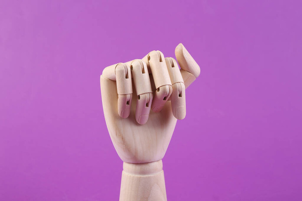Wooden hand folded into fist on purple background - Photo, Image