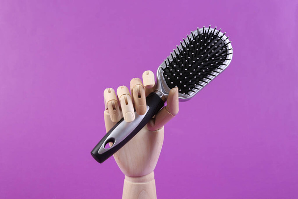 Wooden hand holding a hairbrush on purple background - Photo, Image