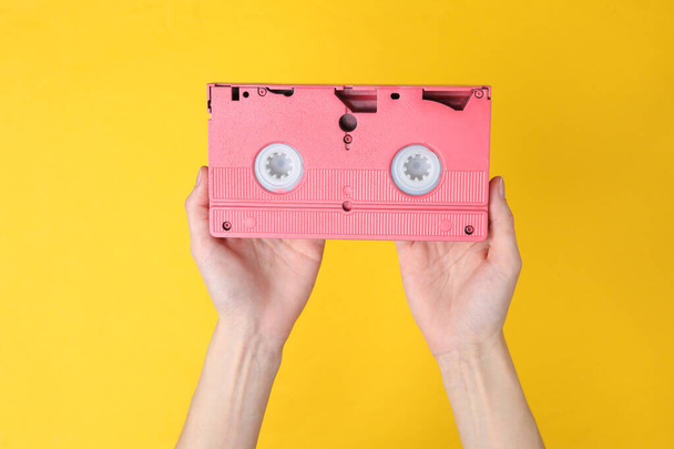 Hands holding retro video cassette on yellow background - 写真・画像