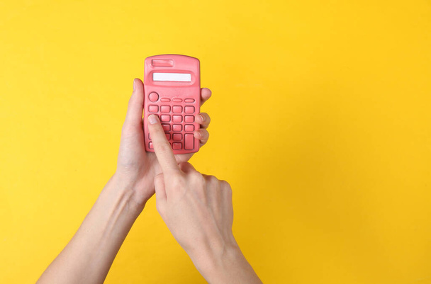 Manos usando calculadora rosa sobre fondo amarillo. Minimalismo - Foto, Imagen
