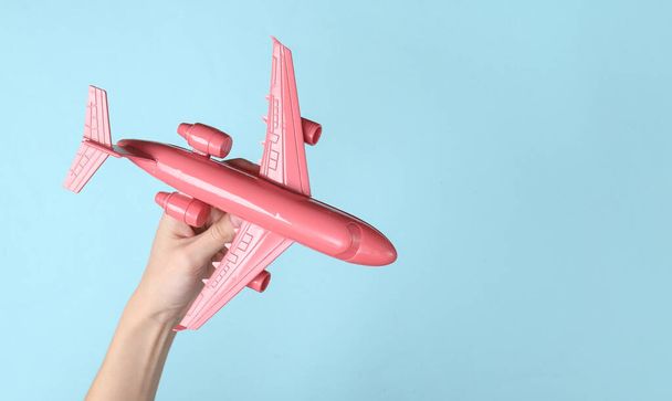 Hand holding pink air plane on blue background. Minimalism travel concept - Photo, Image