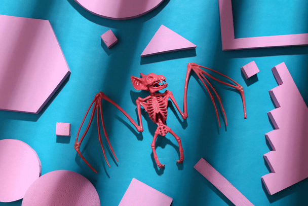 Squelette de chauve-souris rose aux formes géométriques sur fond bleu avec ombre rayée tendance. Mise en page créative. Vue du dessus - Photo, image