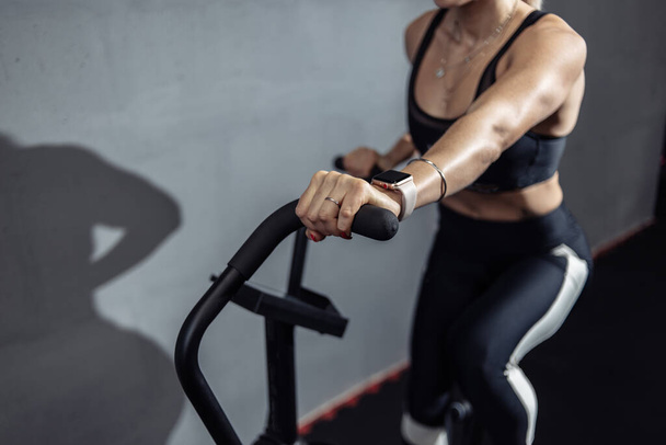 Mujer haciendo entrenamiento cardio intenso en bicicleta estática. Fitness femenina que utiliza la bicicleta neumática para entrenamiento cardiovascular en el gimnasio - Foto, Imagen