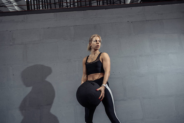Sportowiec robi ćwiczenia rozciągające z piłką medyczną. Muskularna kobieta trenująca piłkę fitness na siłowni - Zdjęcie, obraz