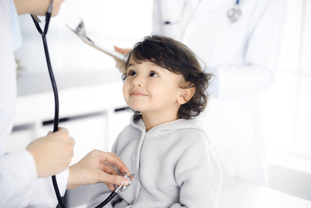 Woman-doctor examining a child patient by stethoscope. Cute arab toddler at physician appointment. Medicine concept - Photo, Image