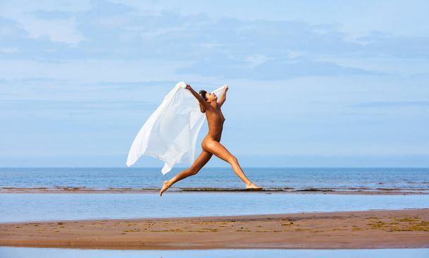 Junge nackte Blondine posiert an einem sonnigen Sommertag an der Küste, ein weißer Stoff flattert im Wind. Sexy Frau genießt die Sommerzeit - Foto, Bild