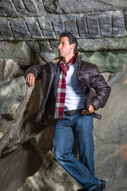 黒い茶色の革のジャケットを着て、長い赤いパターンのスカーフ、ハンサムな中年の男は岩のそばに立って、リラックスして考えています - 写真・画像