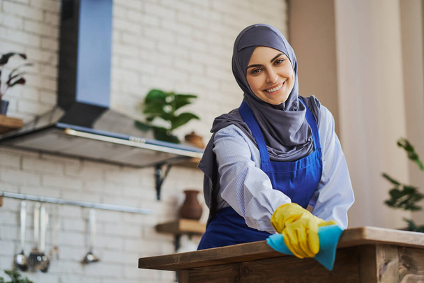 Beautiful Arabian housewife cleaning her house with a rag and gloves - Valokuva, kuva