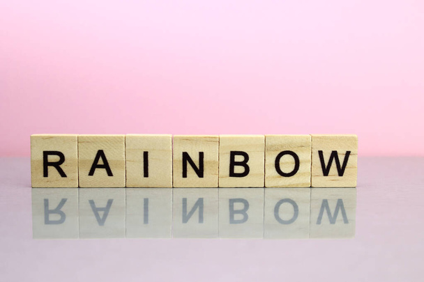 Regenboog woord gemaakt van houten letters op een roze achtergrond - Foto, afbeelding
