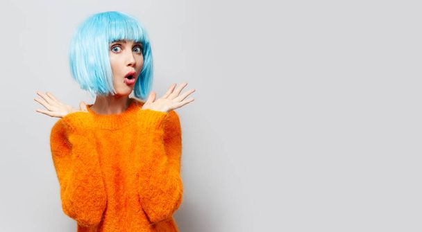 Studio portrait of surprised girl with blue wig, isolated on grey wall. - Photo, Image