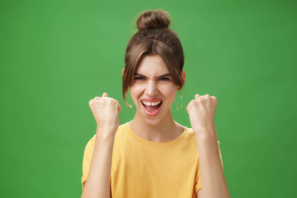 Femme avec l'esprit du gagnant levant les poings serrés souriant excité et encourageant acclamations être prêt pour la salle de gym excercisé stimulant confidents avec crier regardant audacieux caméra sur le mur vert - Photo, image
