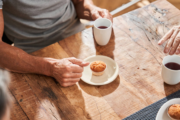 Man holding a cup of tea and preparing to eat the cupcake while having breakfast - Foto, Imagem