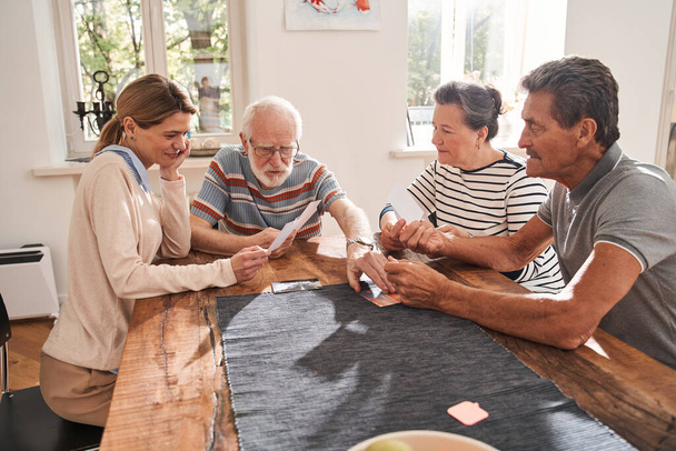 Aide-soignant assis à la table avec des personnes à la retraite et regardant des photos - Photo, image