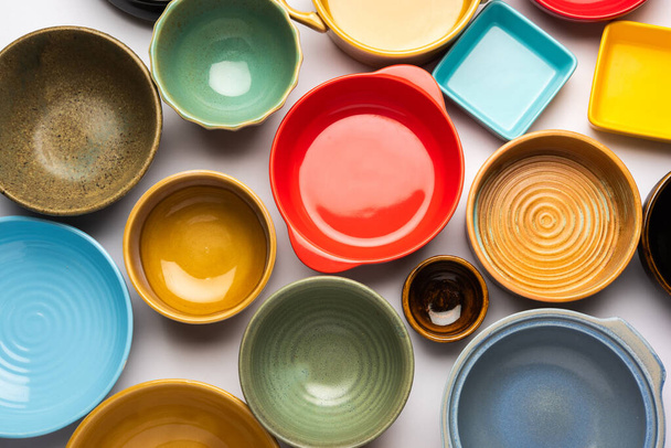 Kolekce prázdných barevných keramických misek. Skupina nádobí zachytil shora, pohled shora, byt ležel na bílém pozadí - Fotografie, Obrázek