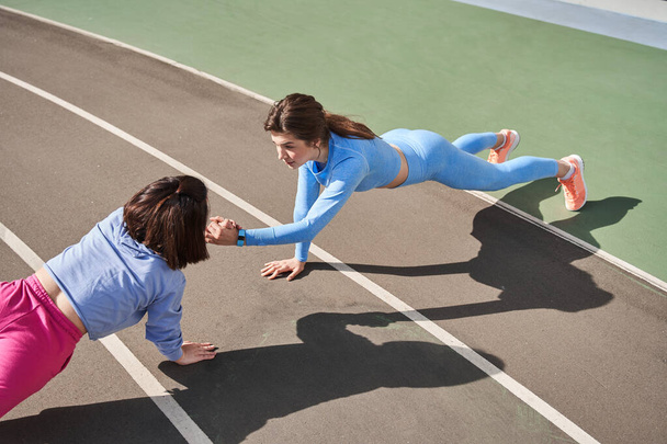 Caucasian girls standing at the plank and holding hands of each other while training - Foto, Bild