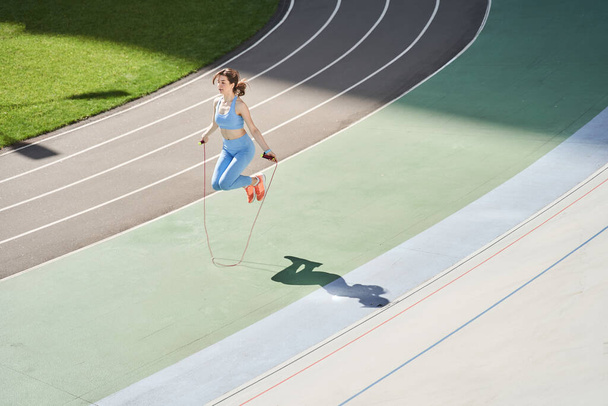 Woman skipping rope during sunny morning on stadium track - 写真・画像