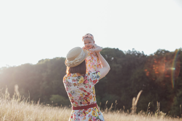 Mother is circling in her arms little happy laughing daughter on summer field, in the rays of sunset - Foto, Bild