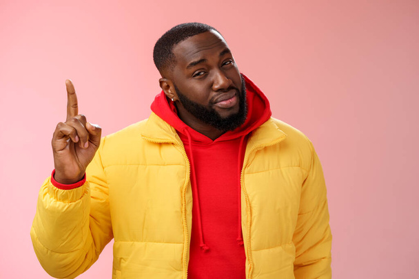 Doubtful displeased african american bearded male customer pointing up index finger squinting cringing disbelief hesitant uncertain product quality, standing questioned frustrated pink background - Foto, afbeelding