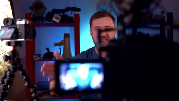 Homme blogueur assis à table avec deux caméras, moniteur rouge et conduit blog vidéo - Séquence, vidéo