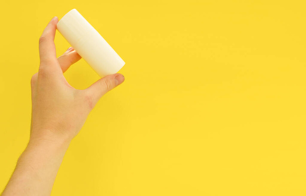 Mão feminina segurando garrafa cosmética branca no fundo amarelo. Faz asneira, copia espaço. Conceito de cuidados com a pele verão - Foto, Imagem