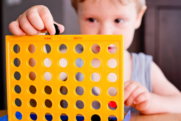 table game connect four. toodler playing game, by inserting checkers in to the grid. concentrated look, raised hand holds the checker. - Photo, Image