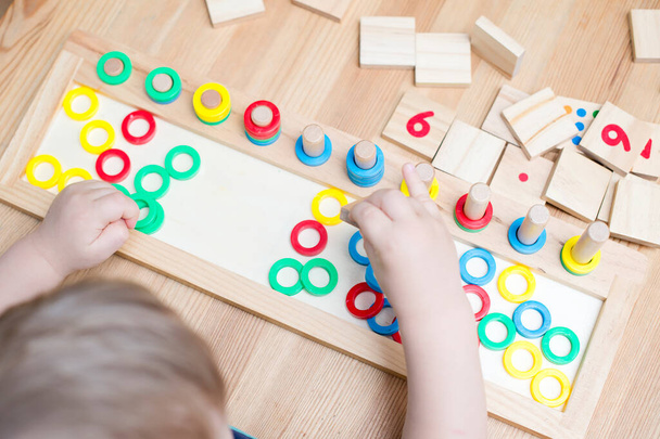 Child playing with different color wooden rings. Sequence, fine motor skills, therapy task for education and brain exercise. Counting math play game. Montessori type implement. Wooden toys. - Fotografie, Obrázek