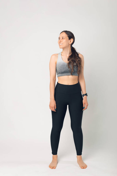 Full length portrait of a young fitness woman in sportswear standing, looking away over white background - Valokuva, kuva