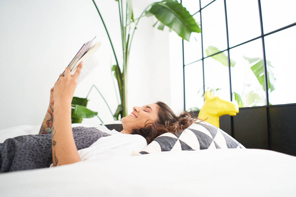 Photo verticale d'une jeune femme lisant un livre dans la salle confortable, tournant la page, apprenant, étudiant, éducation, lisant des livres, concept de rester à la maison et de se détendre. - Photo, image