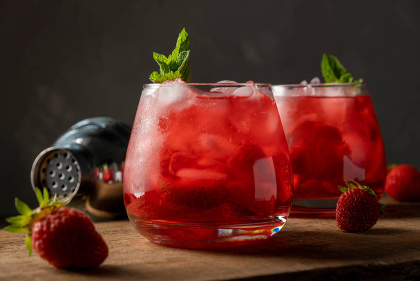 Bebida vermelha com morango, gelo e hortelã. Coquetel de verão refrescante em um copo na mesa de madeira - Foto, Imagem