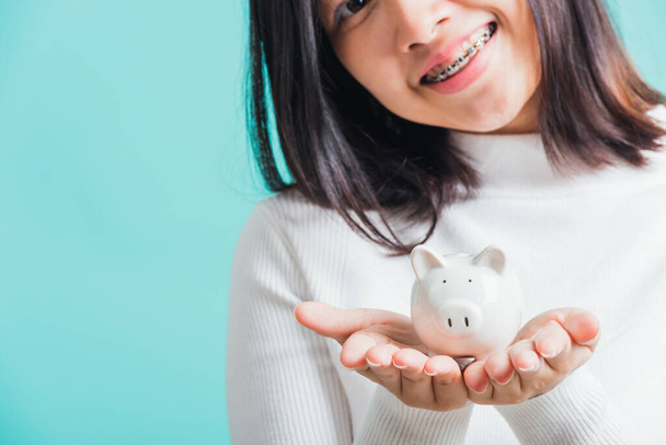Asian beautiful young woman holding piggy bank on hands, portrait relaxation of happy female smiling hold piggybank in palm, studio shot isolated on blue background, concept of saving money - Fotó, kép