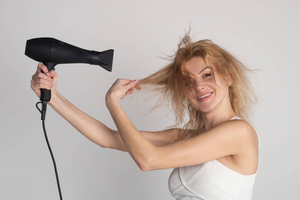 Beautiful caucasian woman posing with wet hair. Women hair treatment. Girl with blonde hair using hairdryer. Hairstyle, hairdressing concept. - Fotó, kép