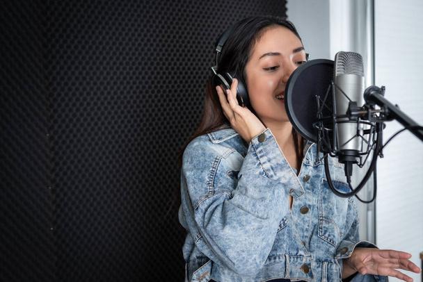 Happy cheerful pretty smiling of portrait of young Asian woman vocalist Wearing Headphones recording a song front of microphone in a professional studio - Photo, Image
