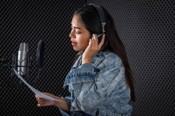 Happy cheerful pretty smiling of portrait of young Asian woman vocalist Wearing Headphones recording a song front of microphone in a professional studio - Фото, изображение