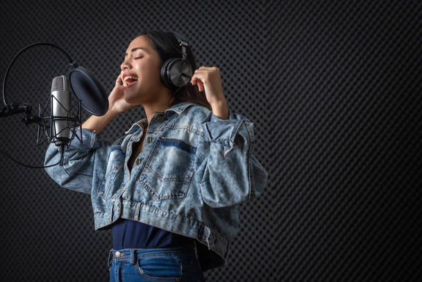 Happy cheerful pretty smiling of portrait of young Asian woman vocalist Wearing Headphones recording a song front of microphone in a professional studio - Фото, изображение