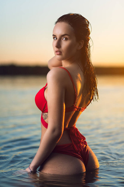 Kırmızı mayo giymiş güzel bir esmer kadın deniz kıyısında dinleniyor. Tropik deniz sahilinde güzel, sıska bir kız. - Fotoğraf, Görsel